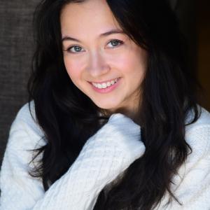 A women wearing a white sweater crosses her arm across her chest and smiles at the camera.