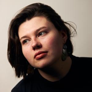 A person with shirt brown hair wearing a black shirt looks of to the side.