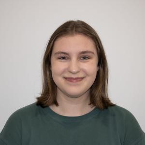 A women wearing a green crewneck stands smiling in front of  white wall 