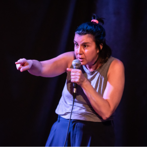 A Fringe artist performs from the stage, holding a mic and pointing at the audience