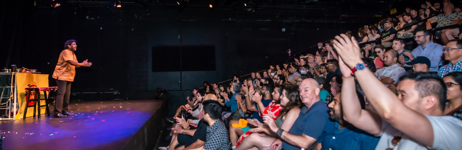A performer bows on stage to a clapping and cheering audience