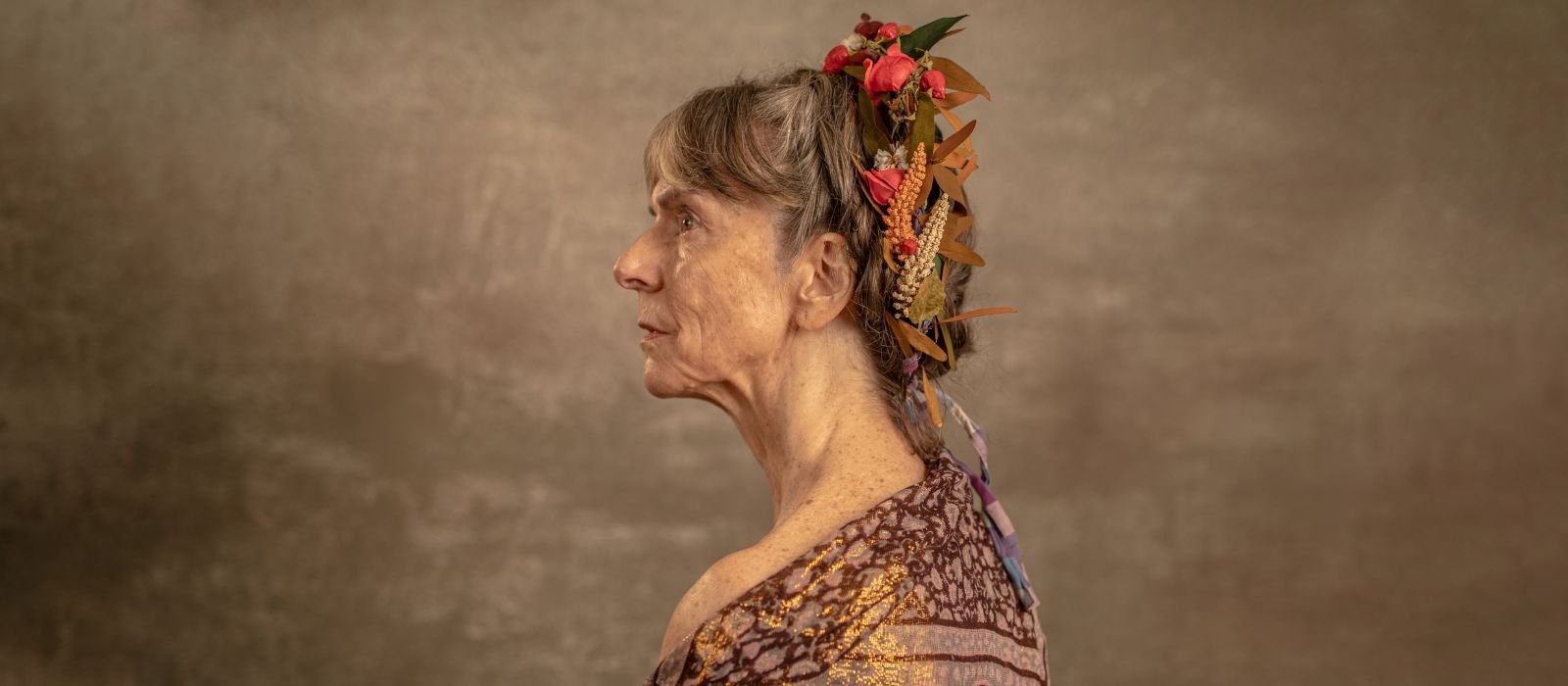 The profile of an older woman, wrapped in a shawl with her hair up in ribbons, against a beige background.