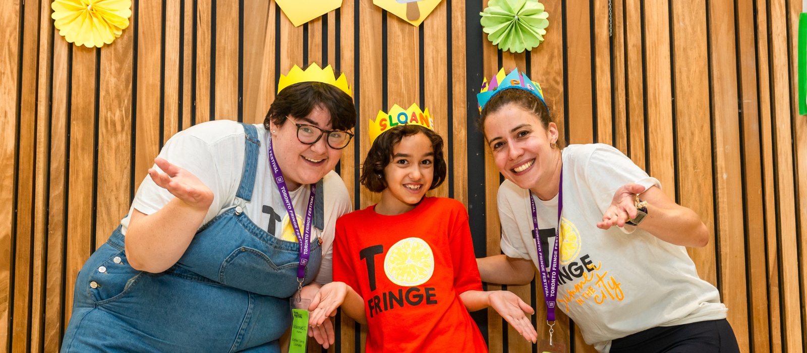 A Fringe Kids Camper wears a handmade crown and smiles between two Camp Counsellors who are also smiling