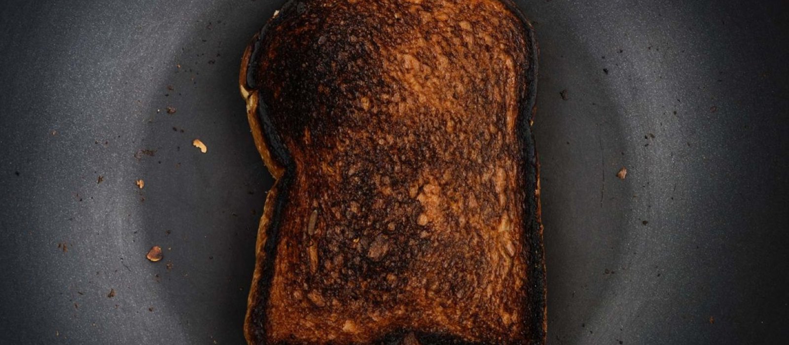 A photo of a piece of burnt toast on a black plate.