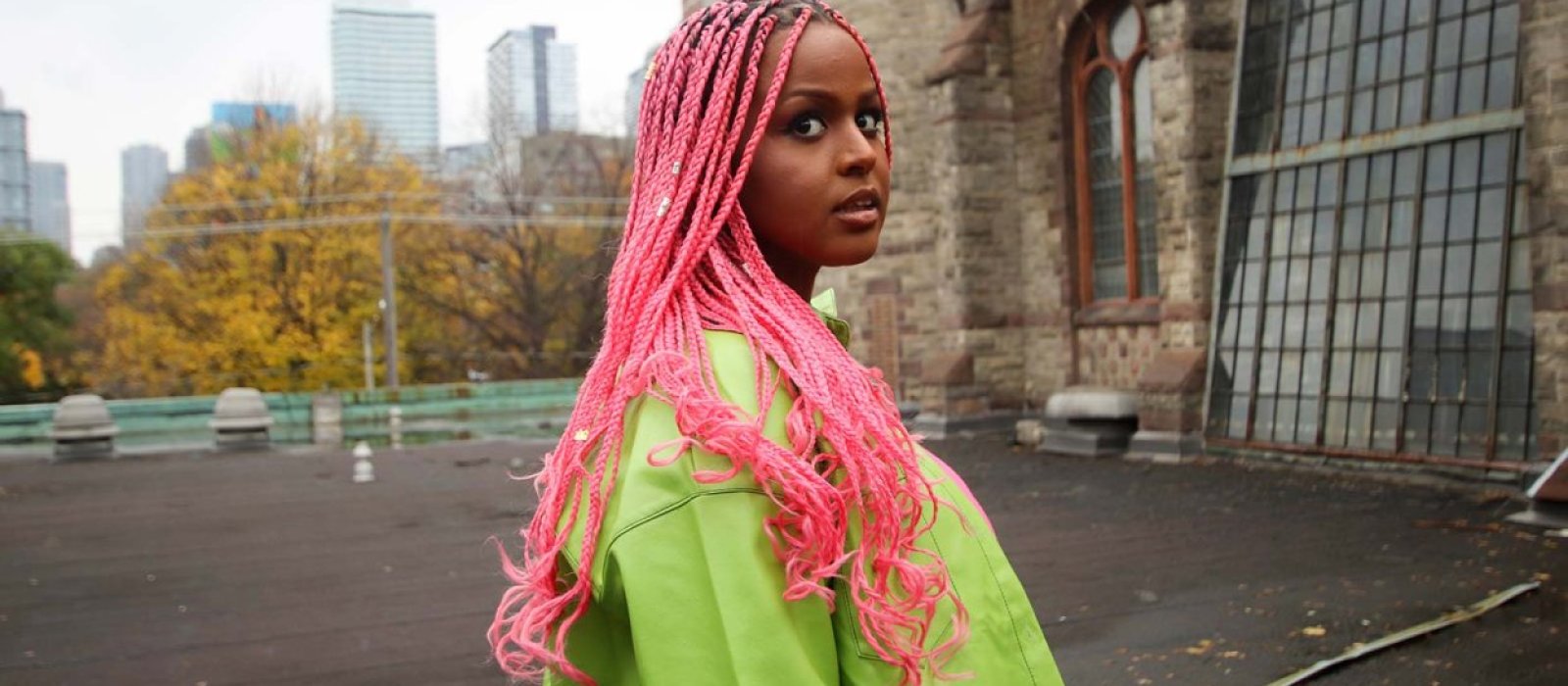 Photo of Fatuma Adar by Graham Isador, outdoors, with pink hair and a bright green jacket.